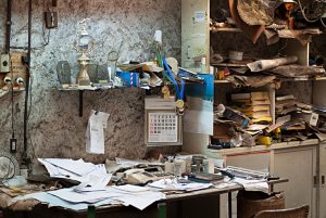 dirty office with books and papers messily stacked on top of desk